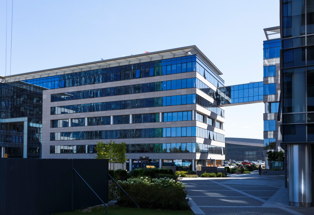 Modern blue-and-white multi-story office building with glass facades and landscaping in foreground.