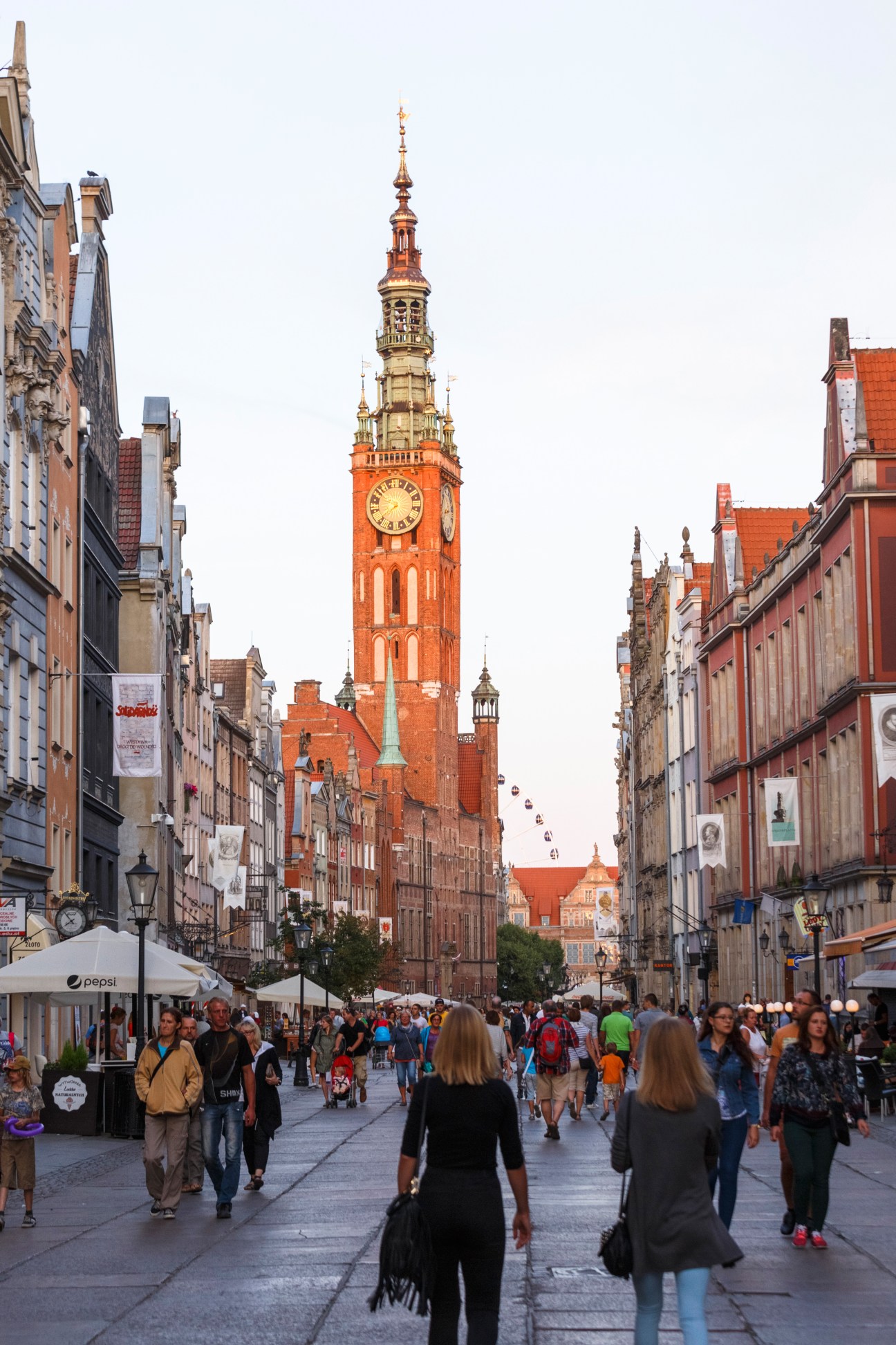 Pedestrians walking through Gdansk's historic city centre with a red brick clock tower and Gothic architecture.