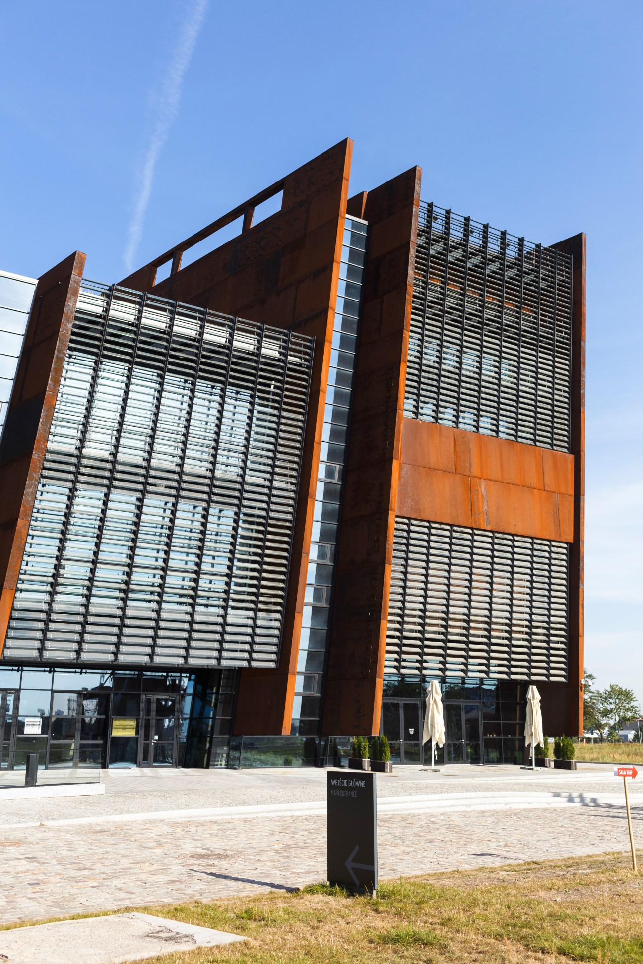 Modern building with rusted steel panels and horizontal louvers under blue sky.