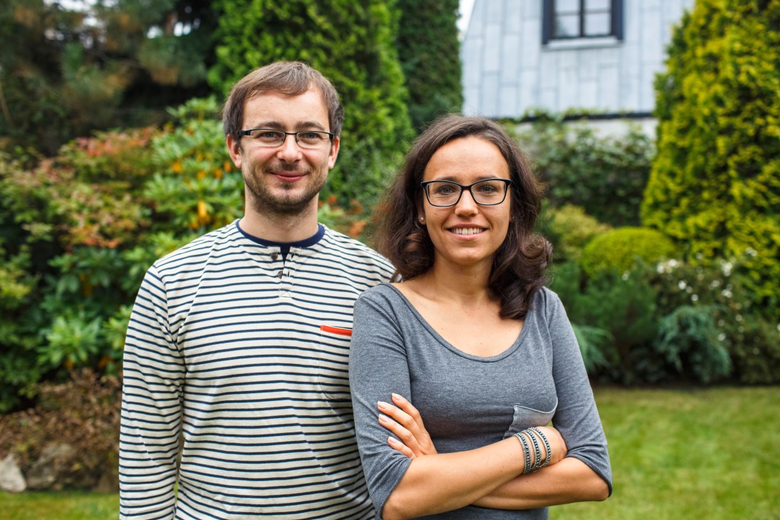 Dominika Bychawska-Siniarska and Jan Siniarski stand in a lush garden with ivy-covered walls behind them.