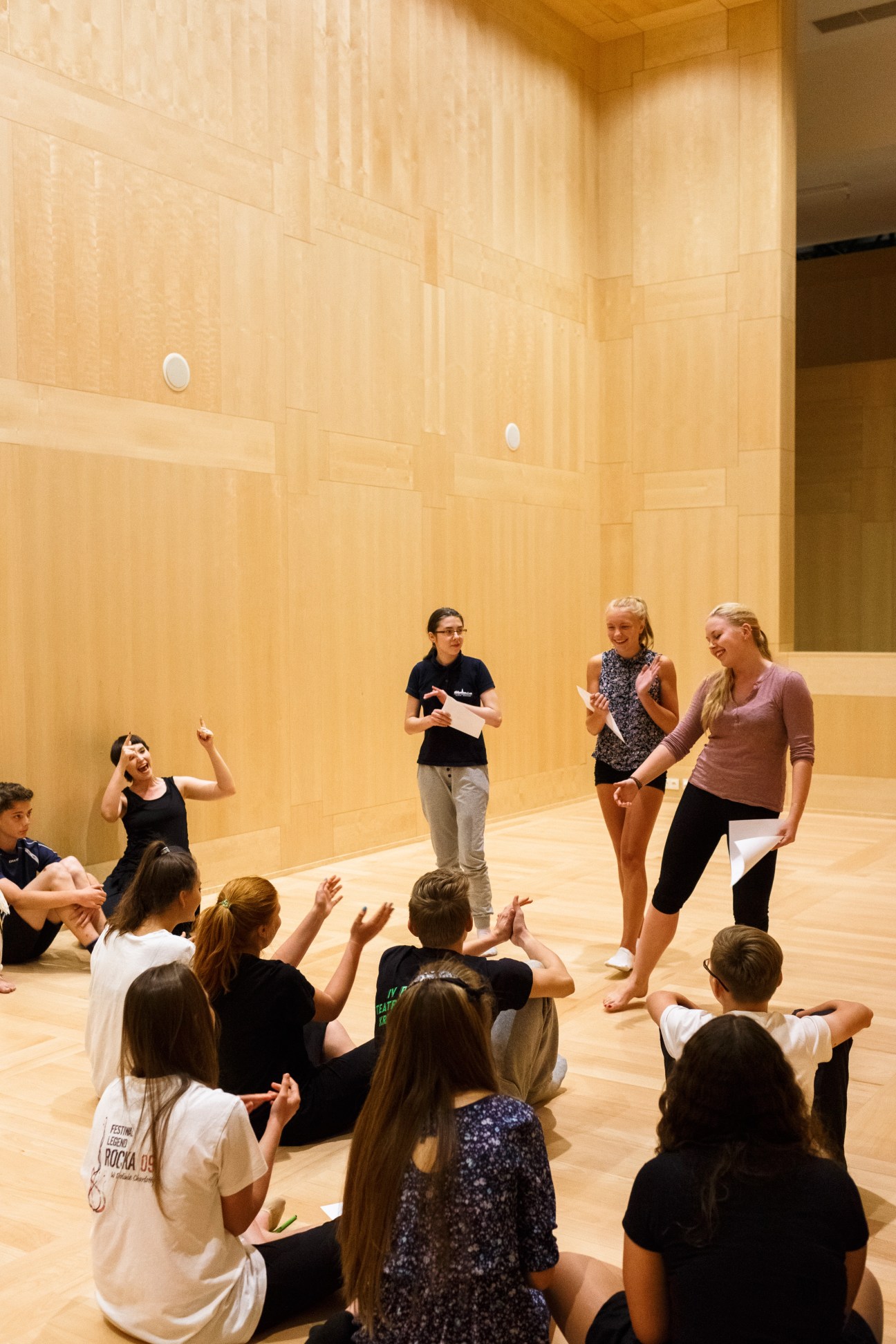 Children sitting on wooden floor in light-filled auditorium at Gdansk's Shakespeare Theatre during a performance or workshop.