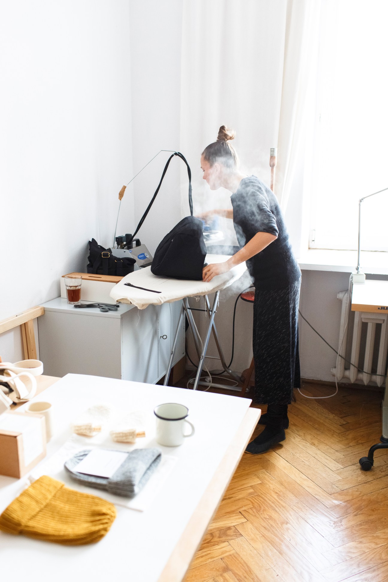 Woman working at a desk with 3D printer and design materials in a bright studio space.