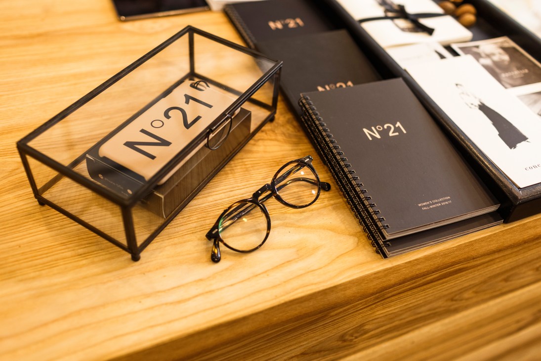 Table display with N°21 branded boxes, glasses, and notebooks on wooden surface.