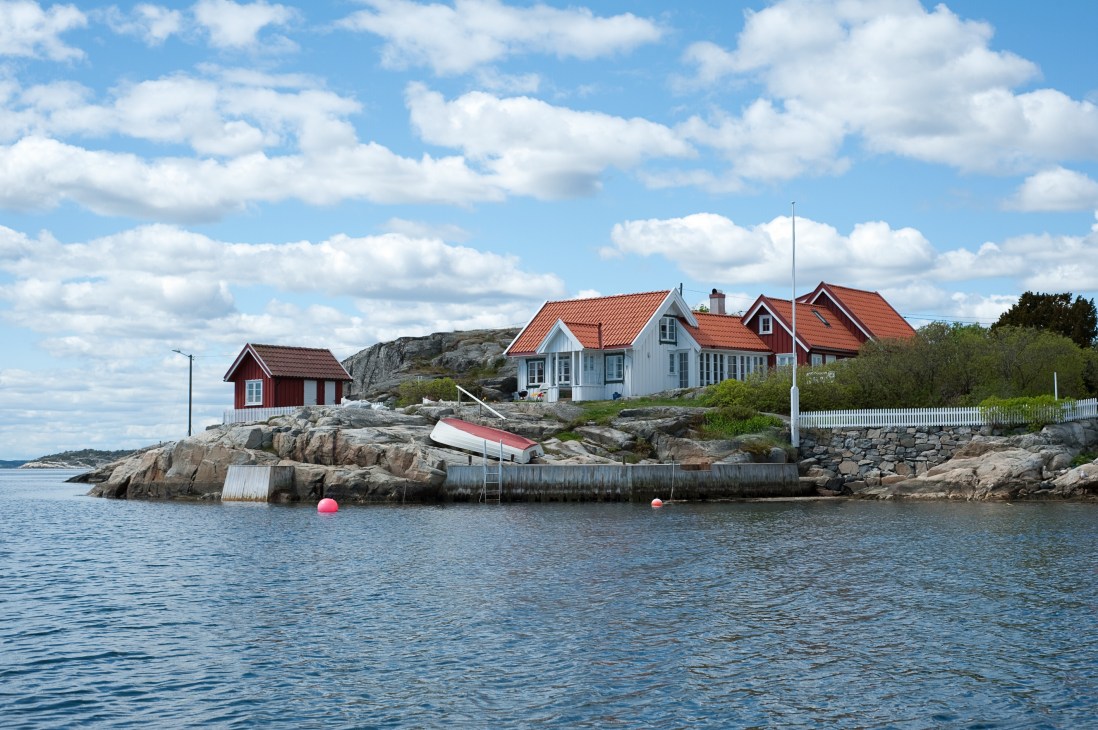 Norwegian coastal houses with red roofs on rocky island overlooking blue water and fjord.