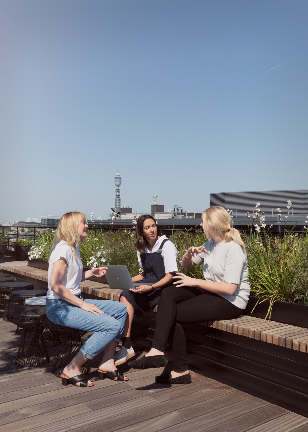 Three women having a meeting on a rooftop garden with the BT Tower visible in the London skyline.