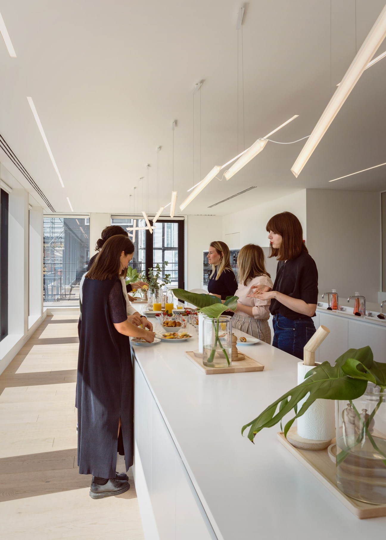 Cos employees gather in a bright, minimalist kitchen area with potted plants, natural light and pendant fixtures.