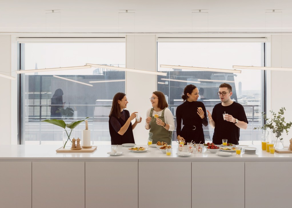 Four Cos communications team members enjoying a fika with pastries and refreshments at a bright kitchen counter overlooking the city.