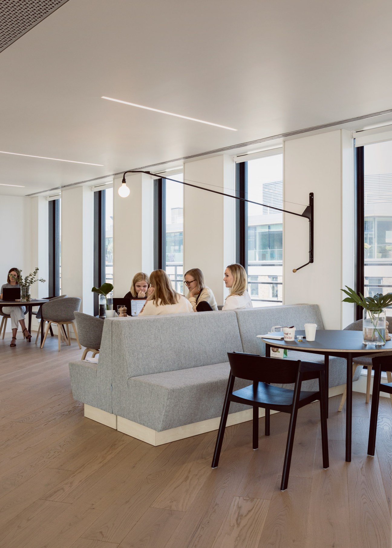 Four women sit on a light gray sofa in a bright, minimalist office space with floor-to-ceiling windows overlooking London.