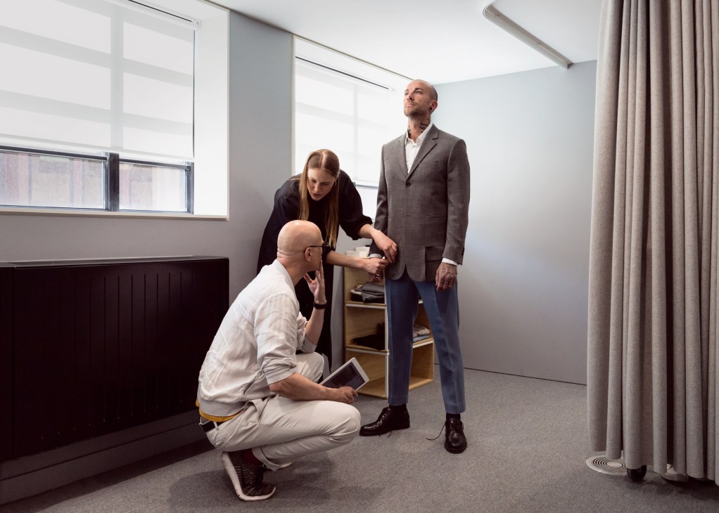 Three people in Cos's men's fitting room examining a prototype jacket on a model.