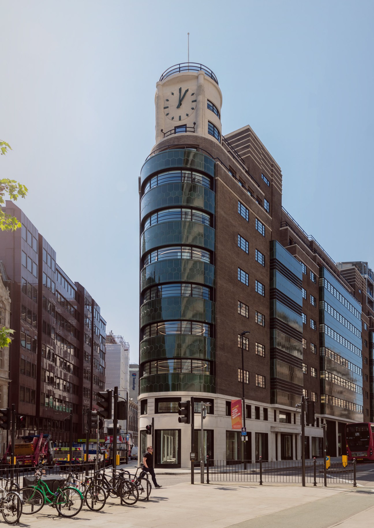 Historic brick building with prominent cylindrical clock tower featuring large clock face and curved glass balconies.