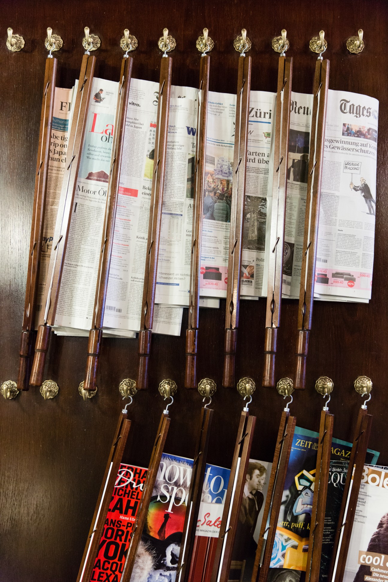 Newspapers clipped to wooden rods with brass finials displayed vertically on dark wood background.