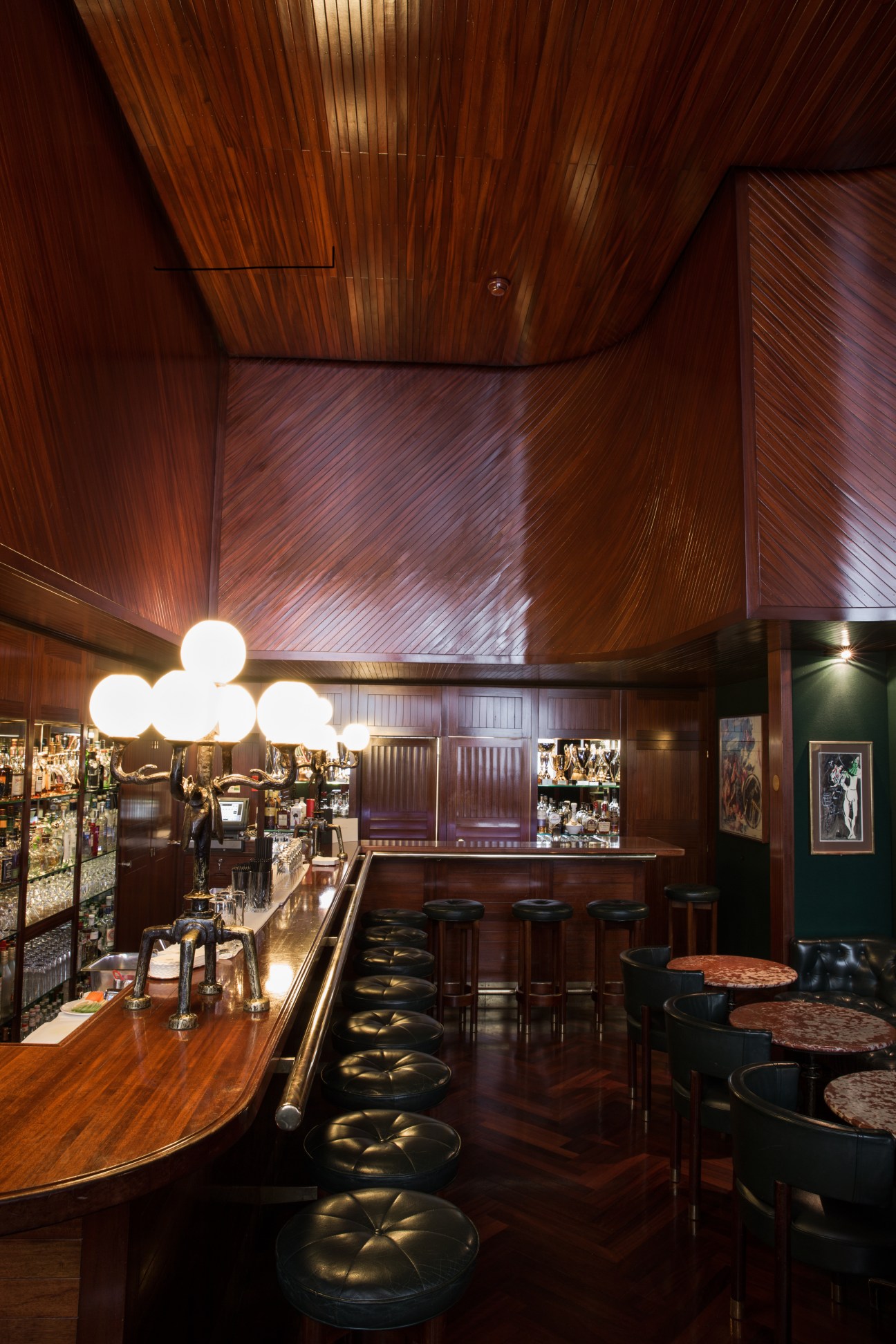 Kronenhalle bar interior with teak wood panelling, spherical Giacometti lamps, and black leather bar stools.