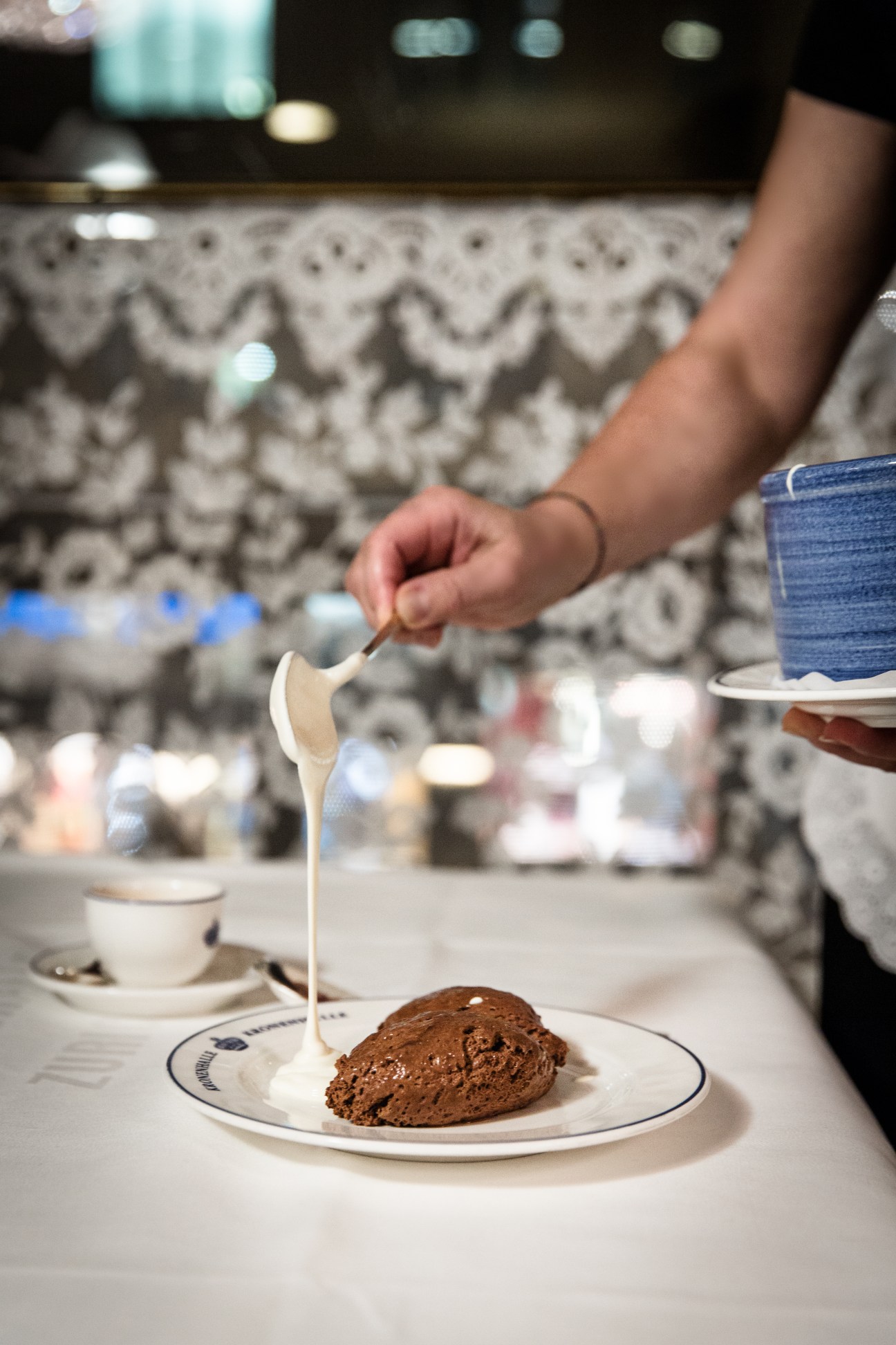 A hand drizzles cream over a chocolate mousse dessert at Kronenhalle restaurant.