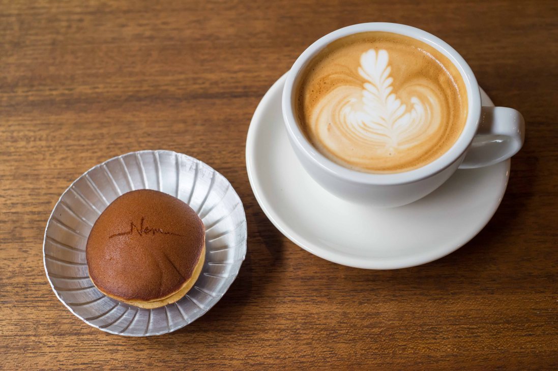 A cappuccino with latte art and a cocoa-dusted pastry on a wooden table at Nem Coffee & Espresso, Tokyo.