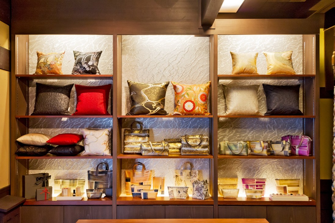 Illuminated display shelves showcasing Hosoo textile cushions, bags and accessories in various colors and patterns.