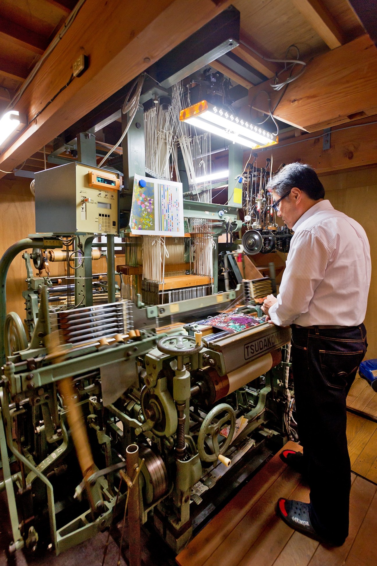 A craftsman operates a traditional weaving loom in a wood-beamed workshop, working on Hosoo textiles.