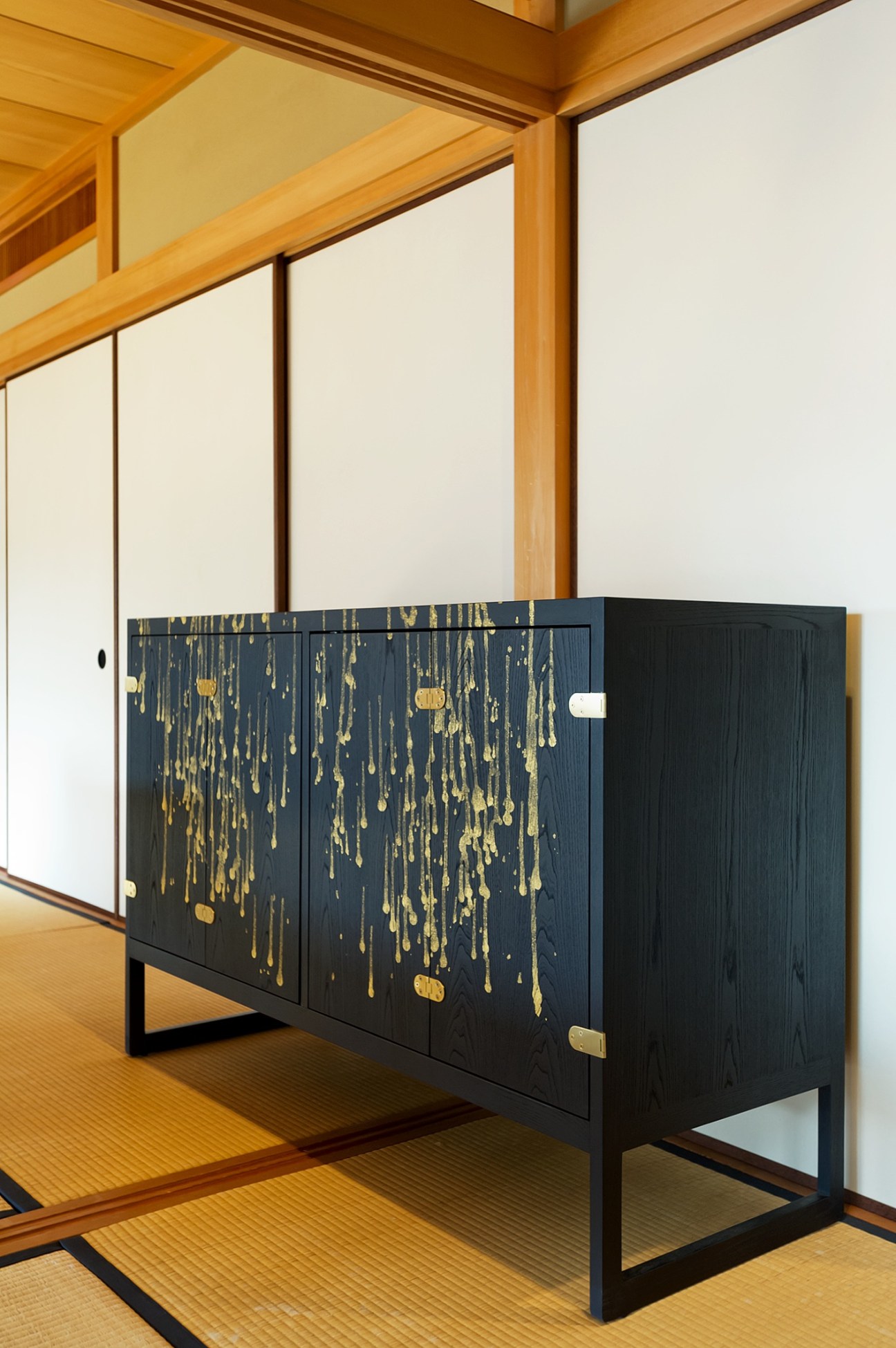Black wooden cabinet with gold chrysanthemum pattern and brass hardware in minimalist interior