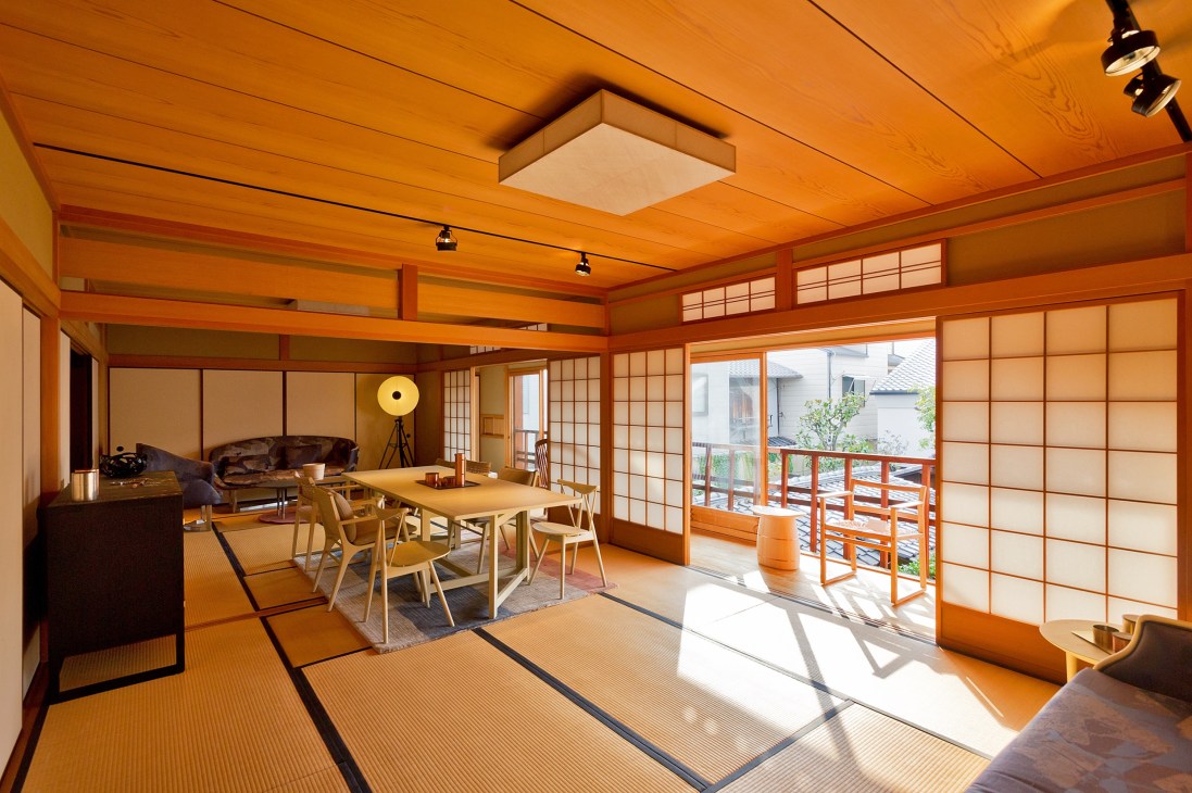Interior of a traditional Japanese wooden showroom with tatami flooring, shoji screens, wooden beams, and modern furniture displayed.