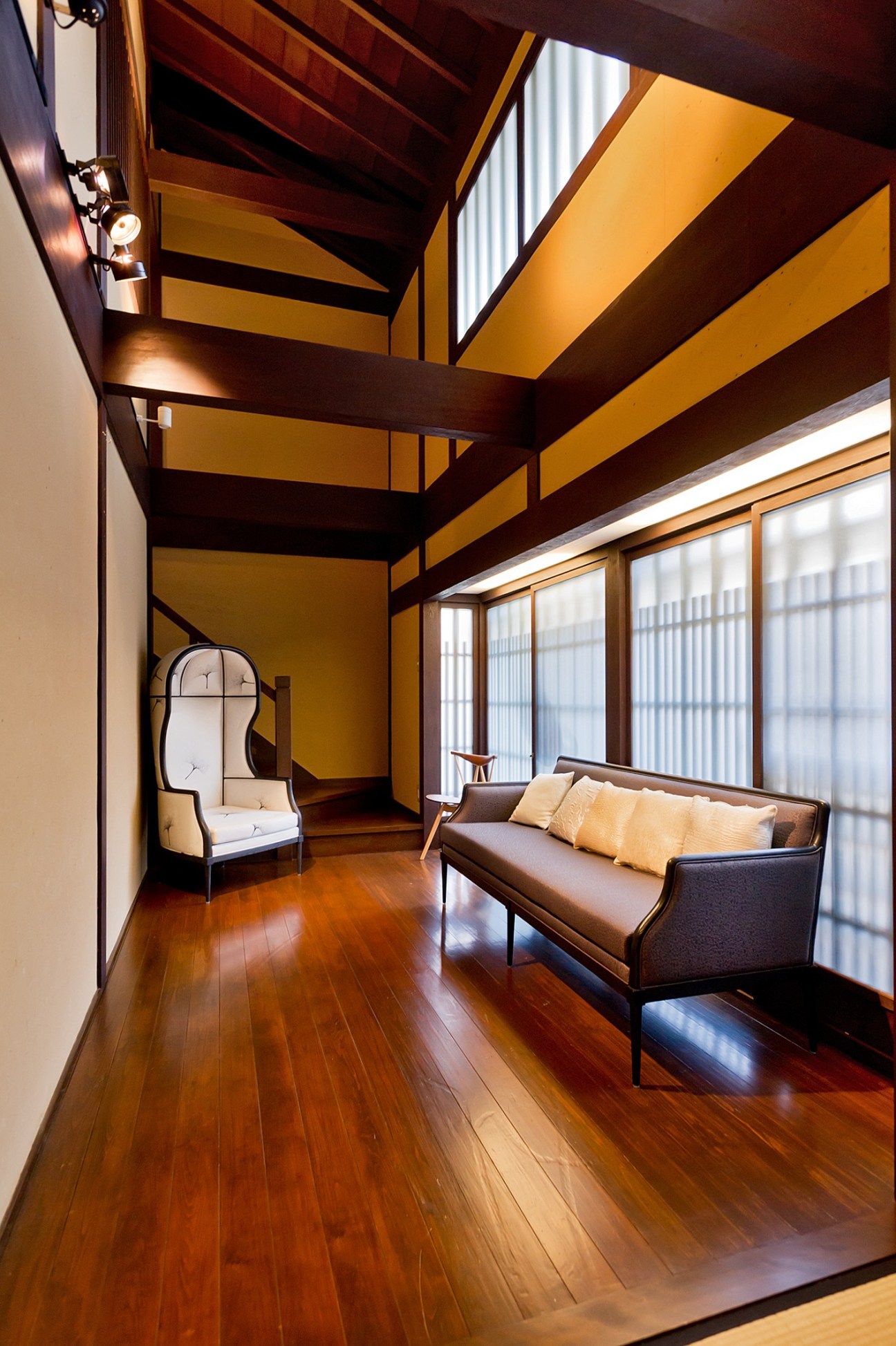 Modern interior space with wooden beams, sofa, chair, and large windows in restored Kyoto showroom.