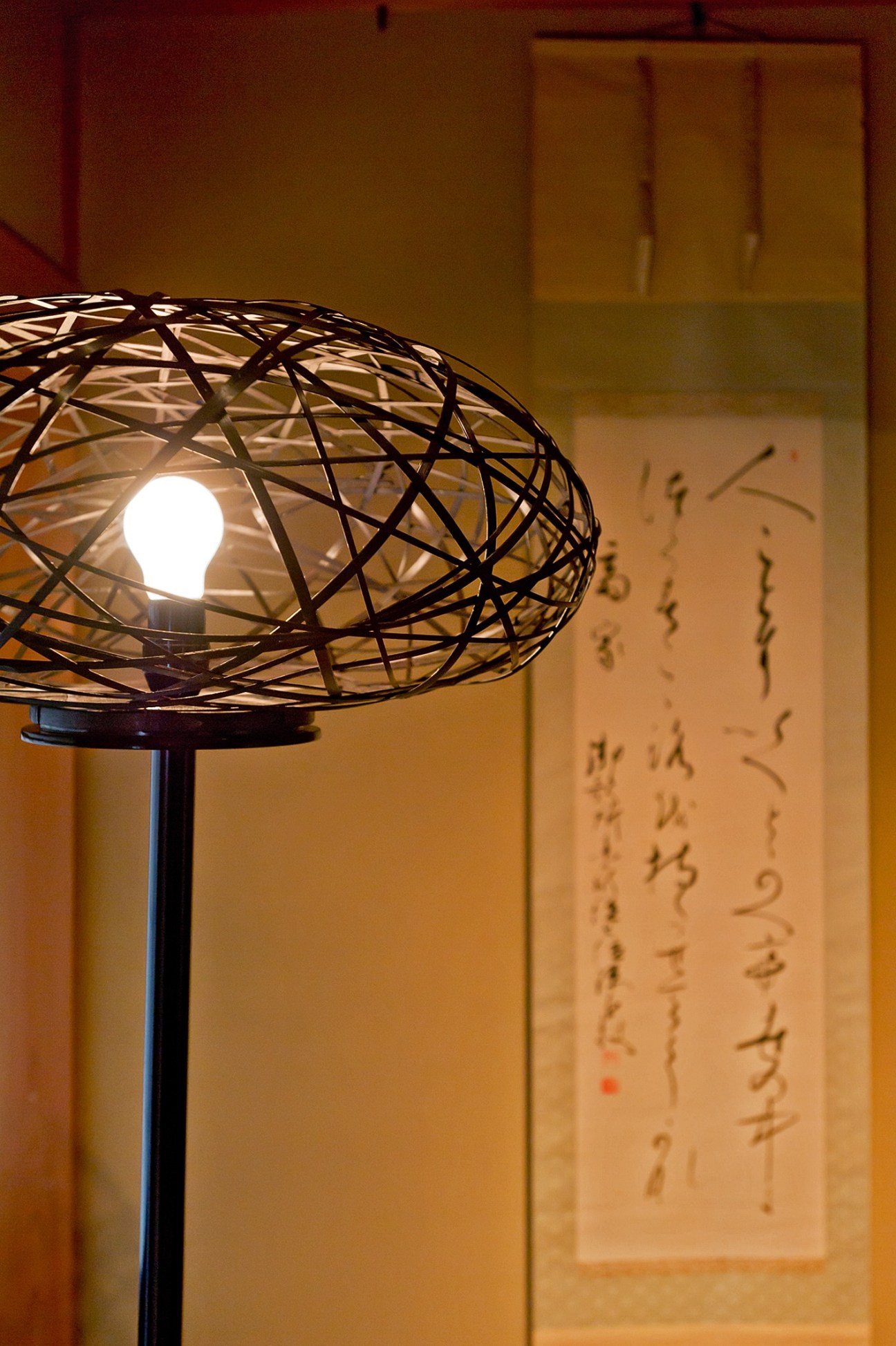 Woven bamboo light shade by Tatsuyuki Kosuga illuminated with a glowing bulb inside.