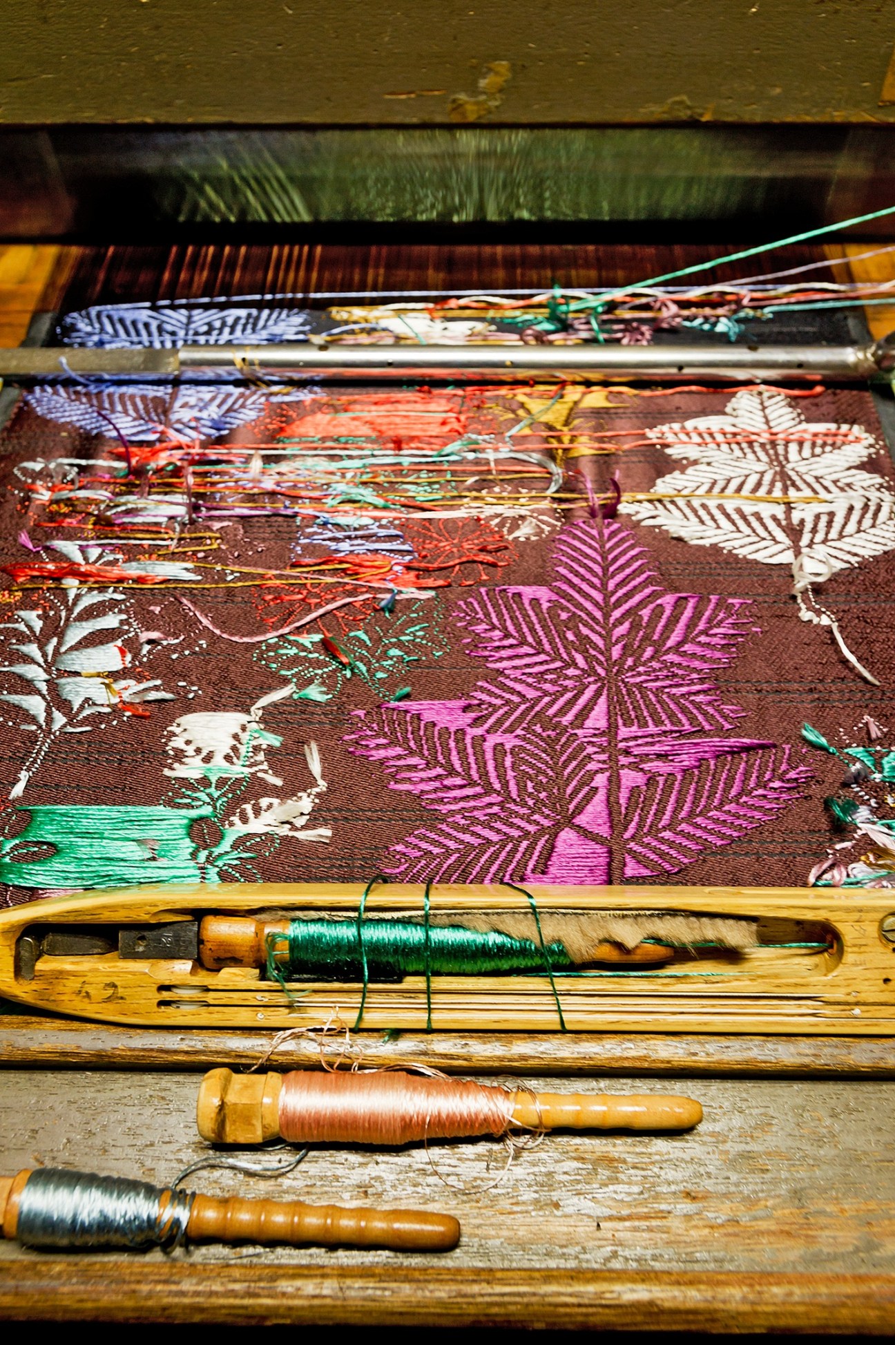 Colorful woven Hosoo textiles on a loom with wooden spools of thread and weaving tools.