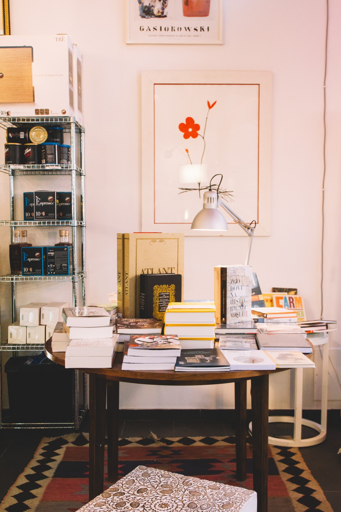 Kul Kul culinary bookshop interior with books on table, shelving unit with coffee supplies, and framed floral artwork.