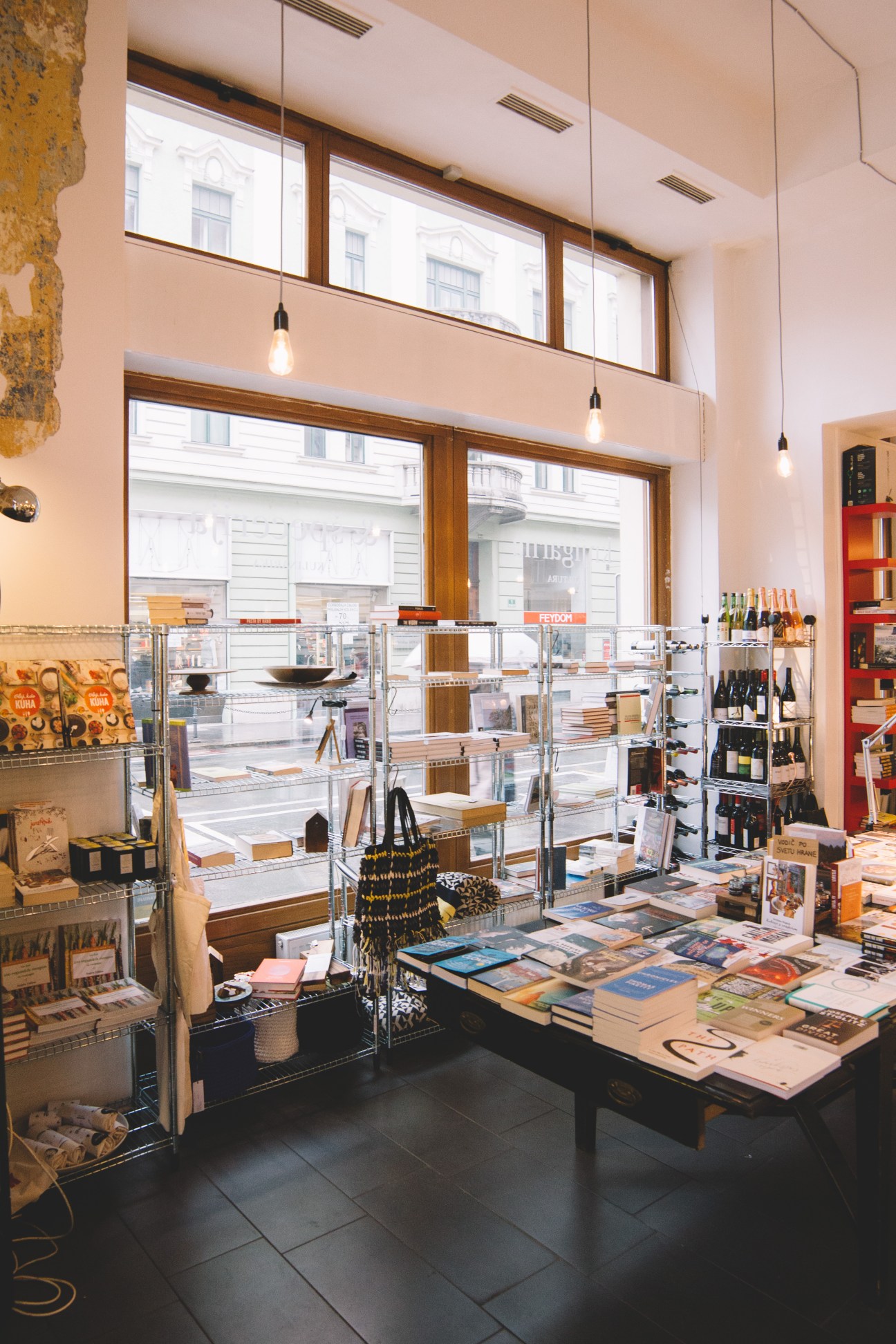 Interior of Kul Kul culinary bookshop with books displayed on tables and shelves, pendant lights overhead, and large windows overlooking the street.