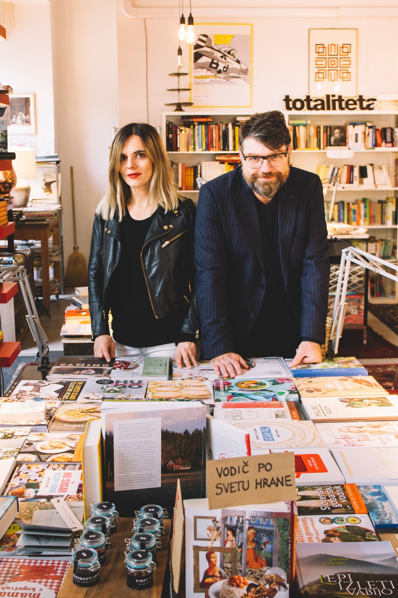 Two people stand behind a table displaying cookbooks and books at Kul Kul bookshop.