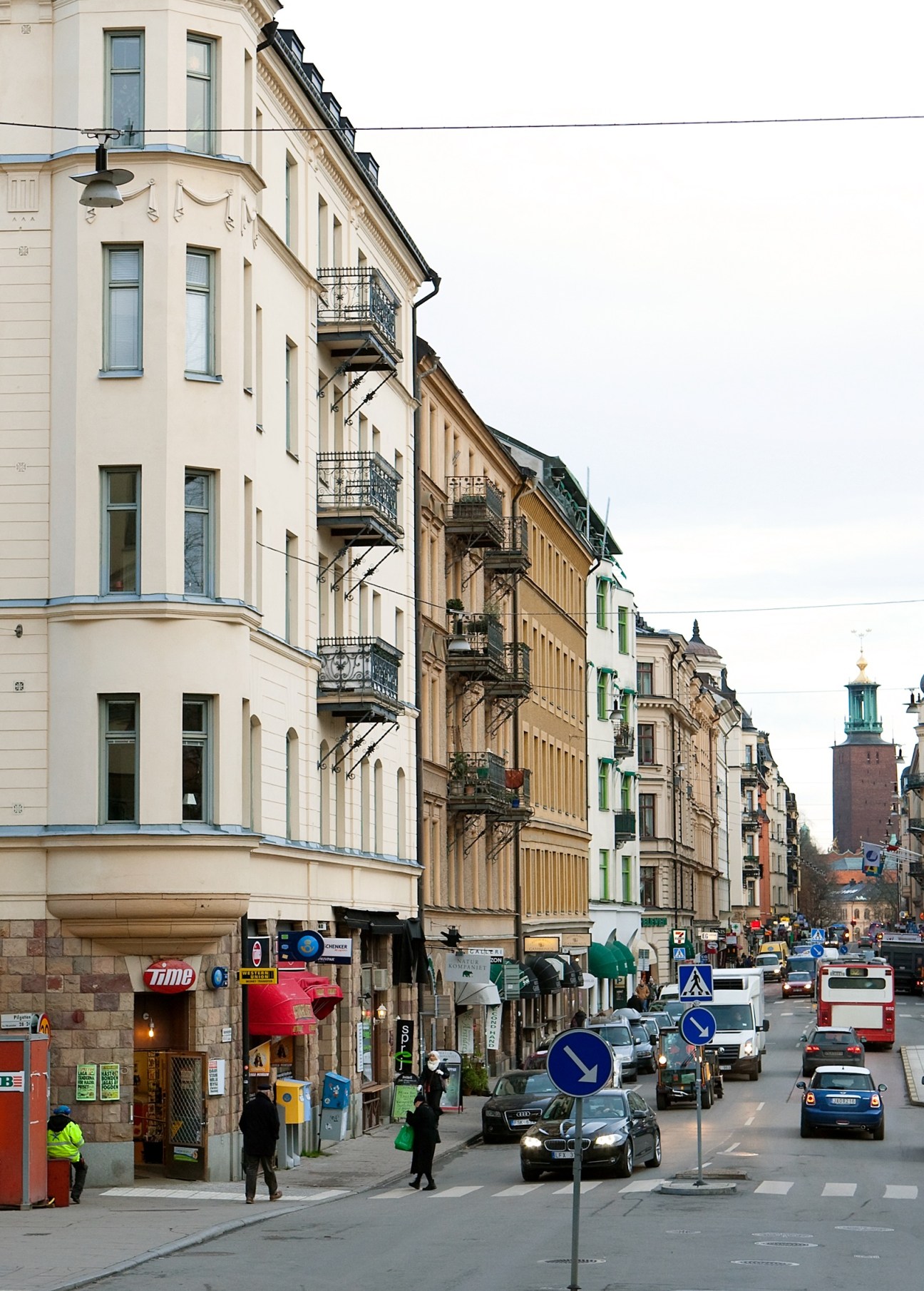 Stockholm street lined with pastel-coloured neoclassical buildings with wrought iron balconies and a church tower visible in the distance.