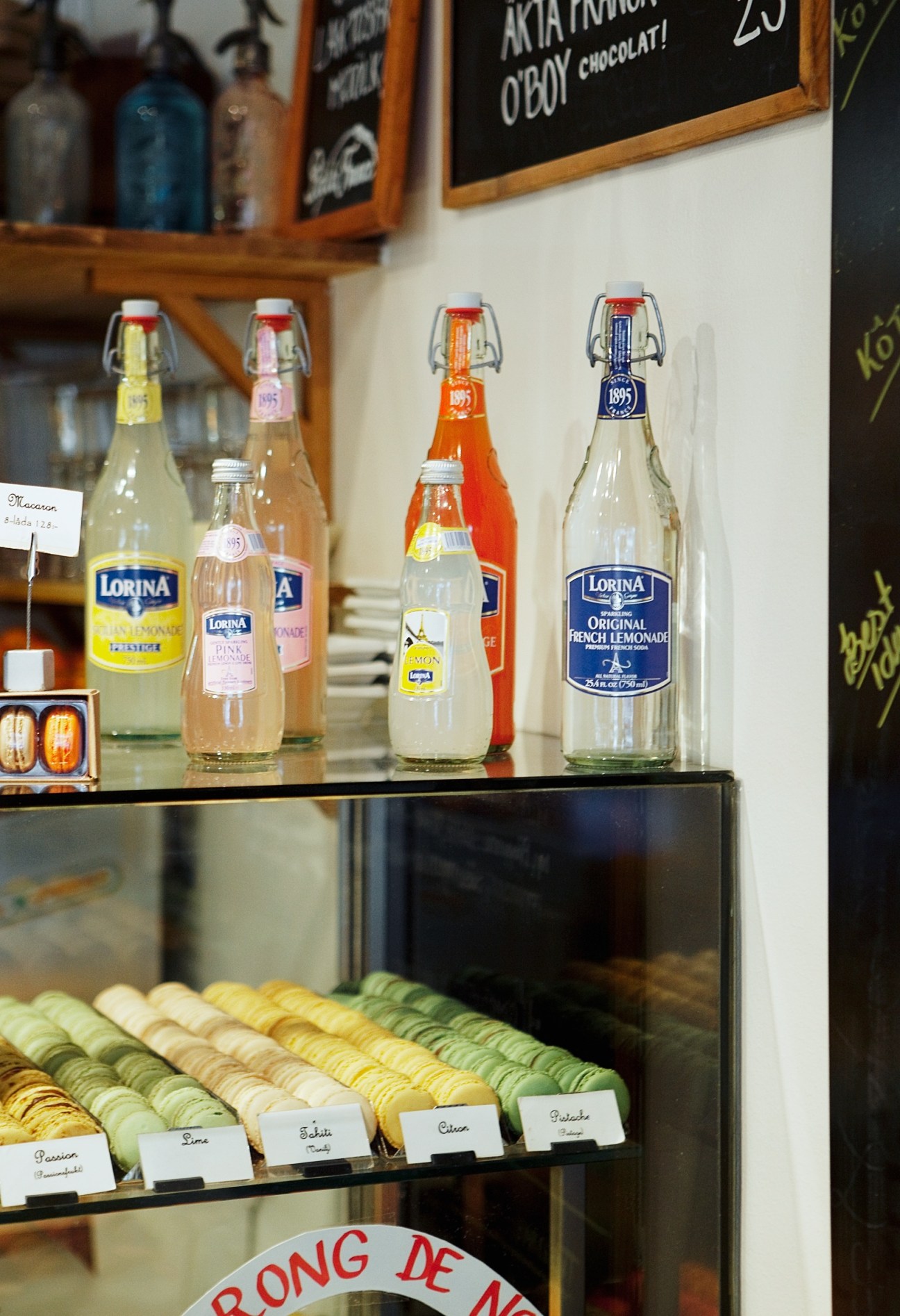 Display window at Petite France bakery showing Lorina bottled drinks and colorful macarons.