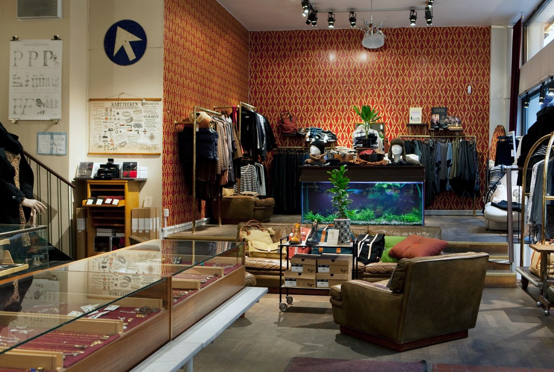 Interior of Grandpa vintage clothing and furniture shop with red patterned wallpaper, clothing racks, and an aquarium display.