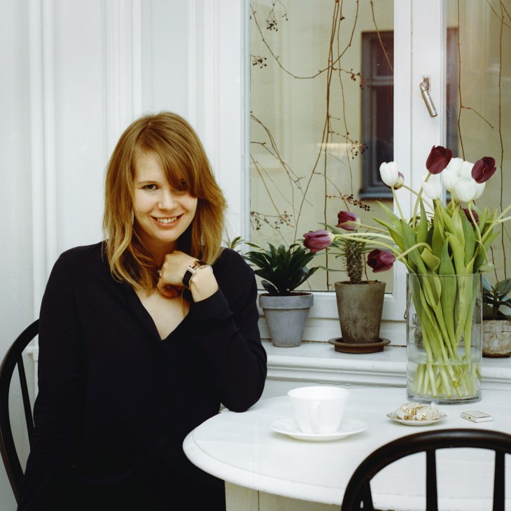 Woman with reddish-brown hair in black top sitting at white table with tulips and potted plants.