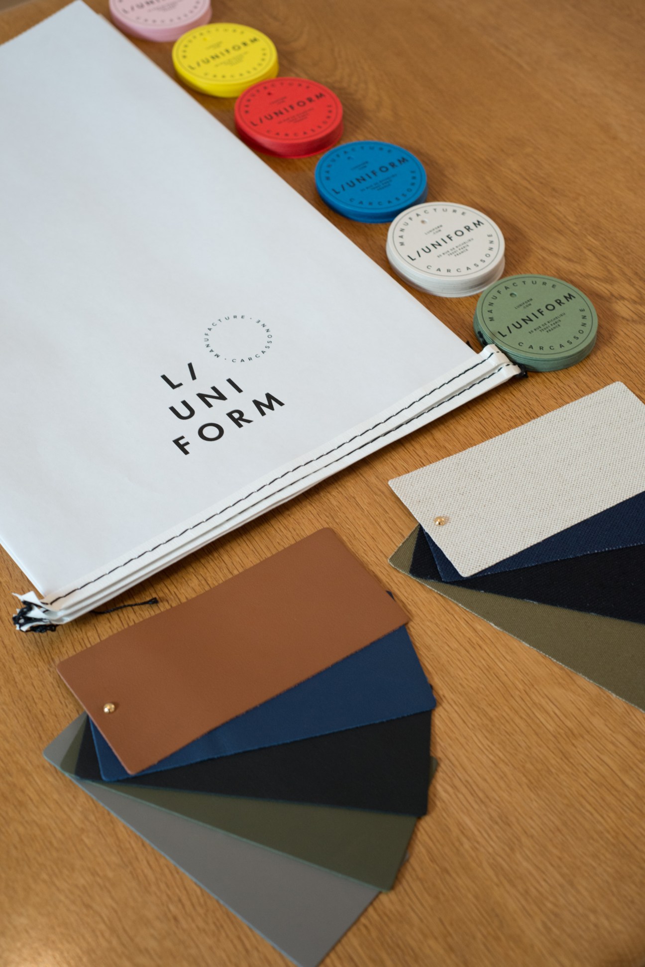 L/Uniform brand swatches showing colored fabric samples and branded wax seals on wooden surface.