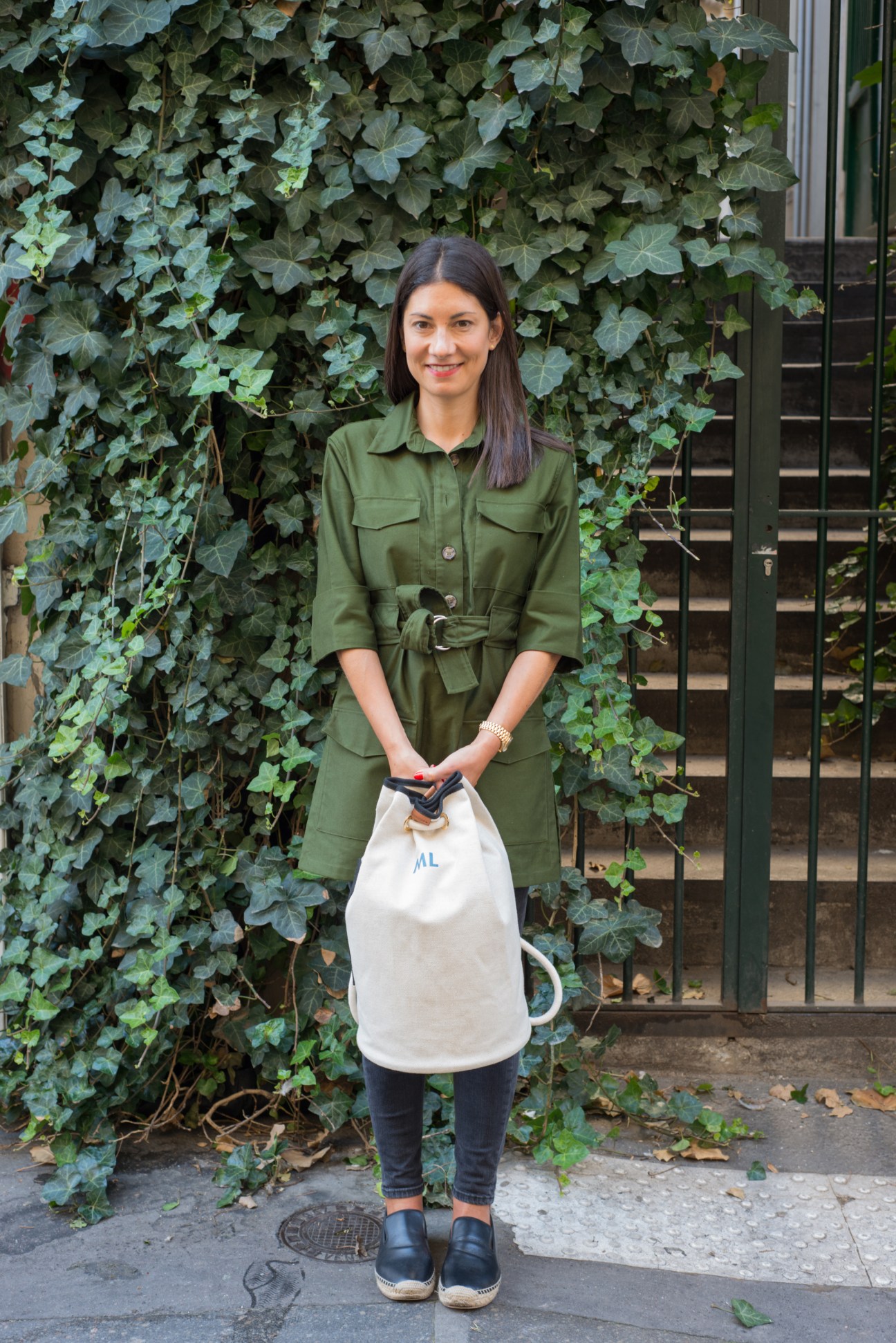 Jeanne Signoles holds a monogrammed L/Uniform canvas bag against an ivy-covered wall.