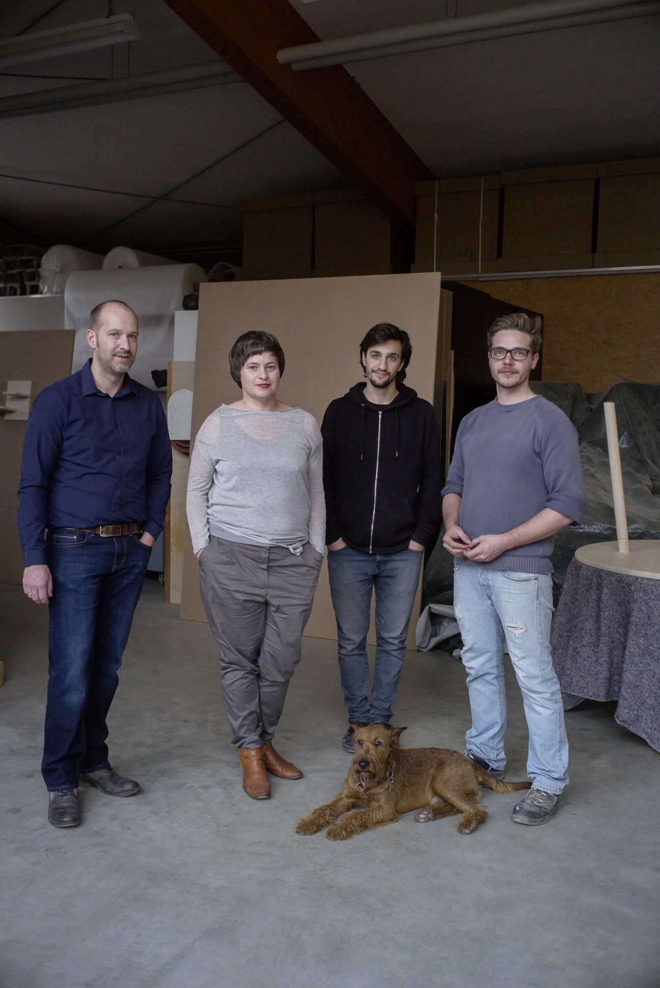 Oliver and Nicola Stattmann, Shay Assas, and Frederik Kötter stand in their workshop with Murphy the dog.