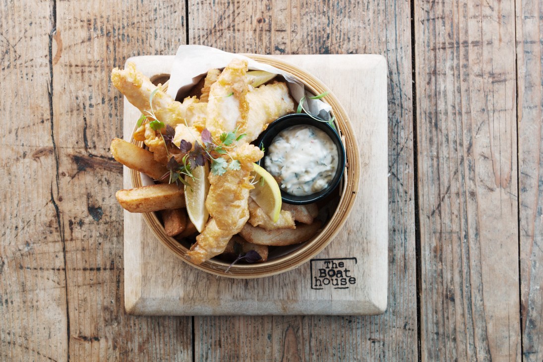 Fish and chips served in a bamboo steamer with tartar sauce and micro-herbs on a wooden board.
