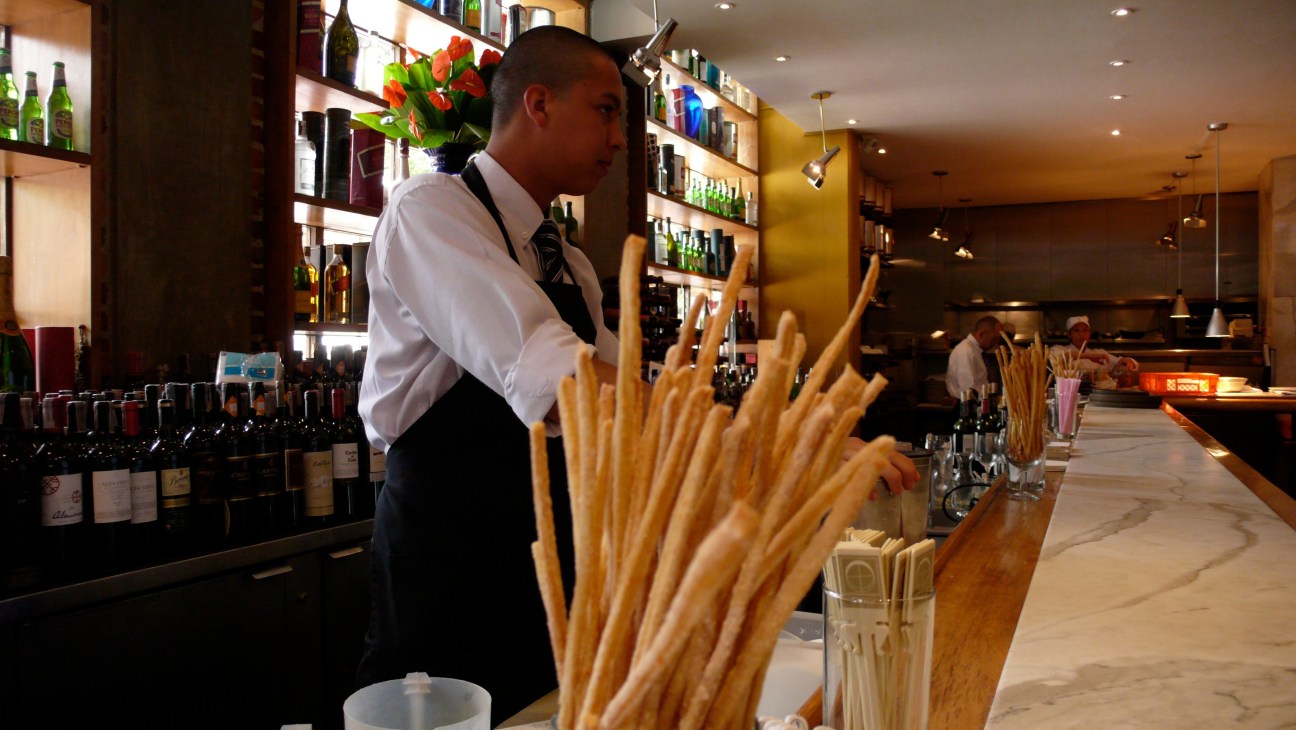 Luna restaurant bar with breadsticks in wooden holder and bartender in white shirt.