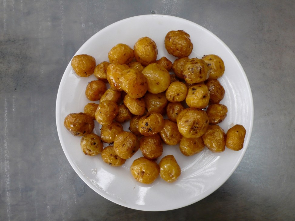 Roasted criolla potatoes on a white plate against a grey surface.