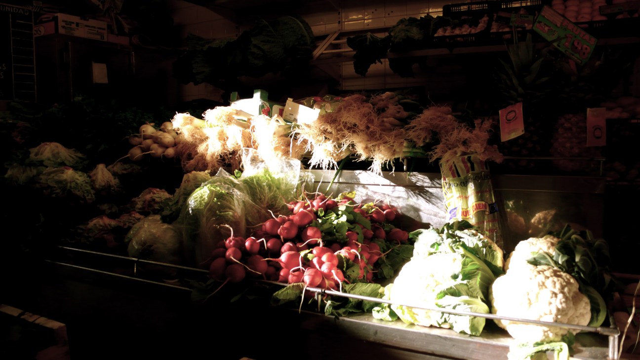 Covered market produce display with radishes, root vegetables and leafy greens under bright lighting in Palma de Mallorca.