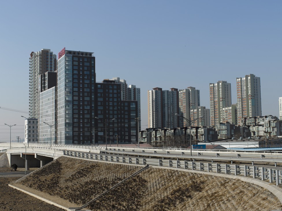 Rows of high-rise apartment blocks stretch across suburban Beijing beyond a concrete bridge and highway.
