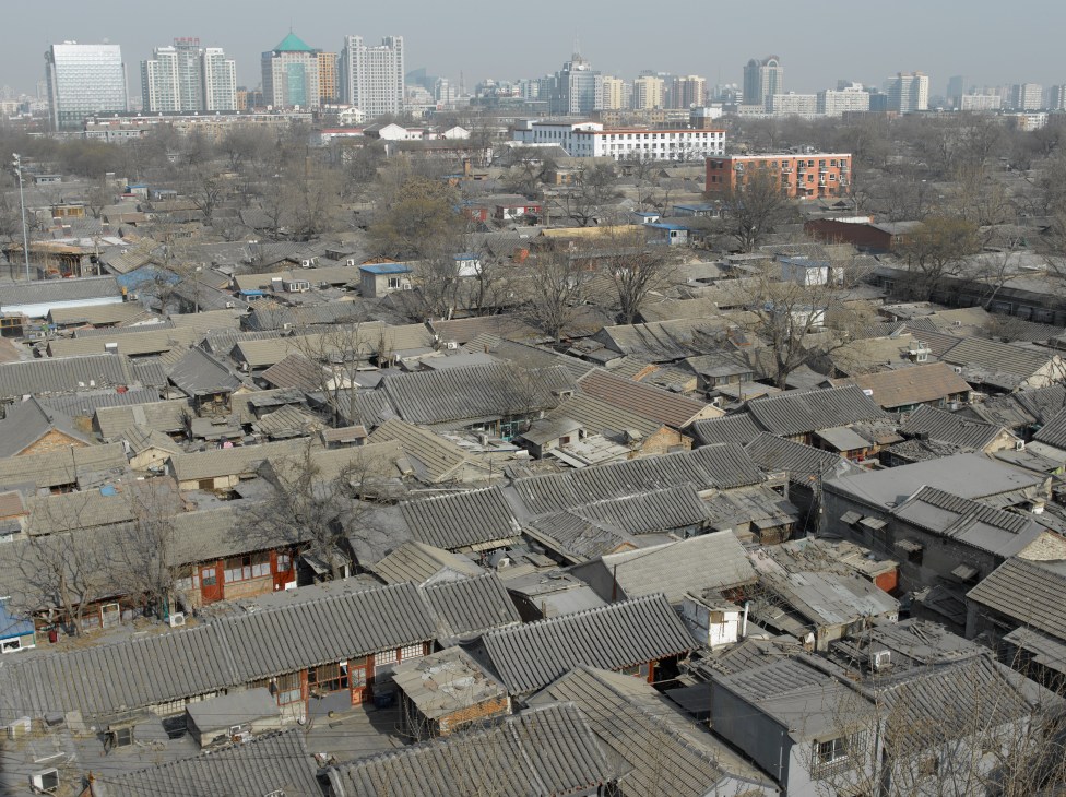 Traditional low-rise hutong neighbourhood with metal roofs contrasting against modern high-rise buildings in Beijing's skyline.