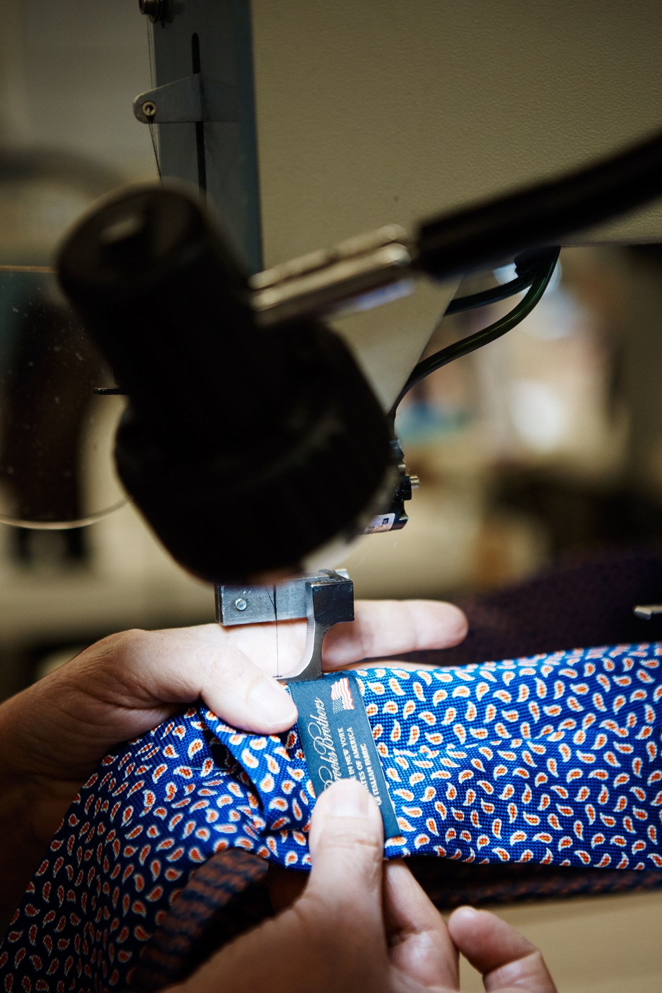Worker attaching clothing labels by hand to blue patterned fabric with sewing equipment.