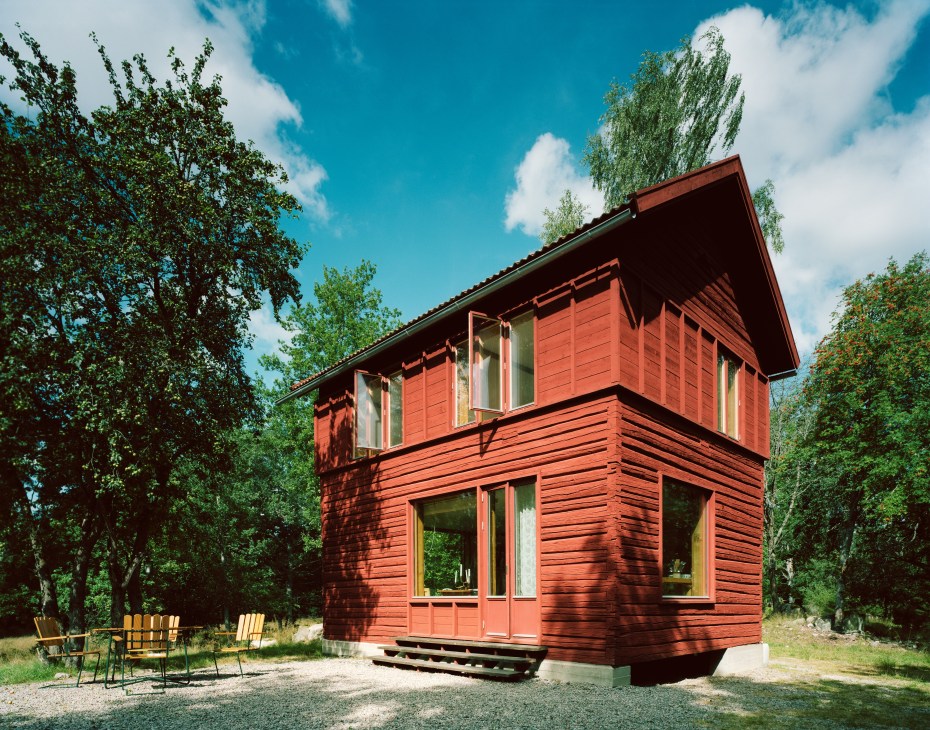Red wooden summerhouse with added timber storey surrounded by trees and outdoor furniture.