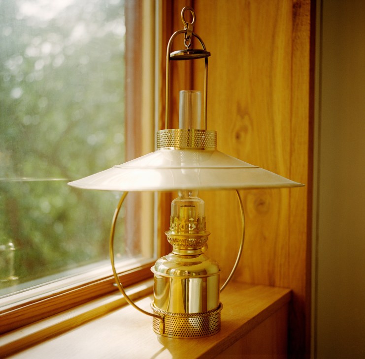 Brass lantern hanging by a window with wooden frame and natural light filtering through.