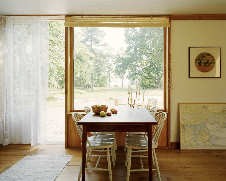 Dining table with brass candlestick and chairs facing large windows overlooking forest and lake.