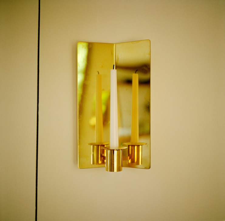Brass Svenskt Tenn candle sconce with mirrored backing holding white candles on pale wall.