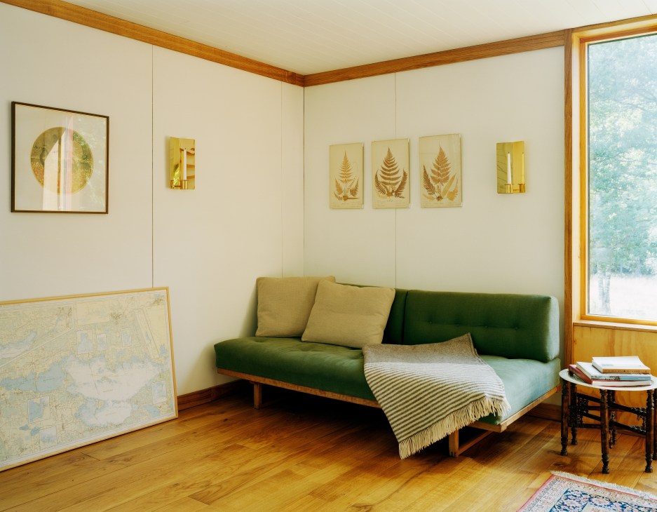 Living room interior with green Børge Mogensen sofa, wooden floors, and framed botanical artwork on cream walls.