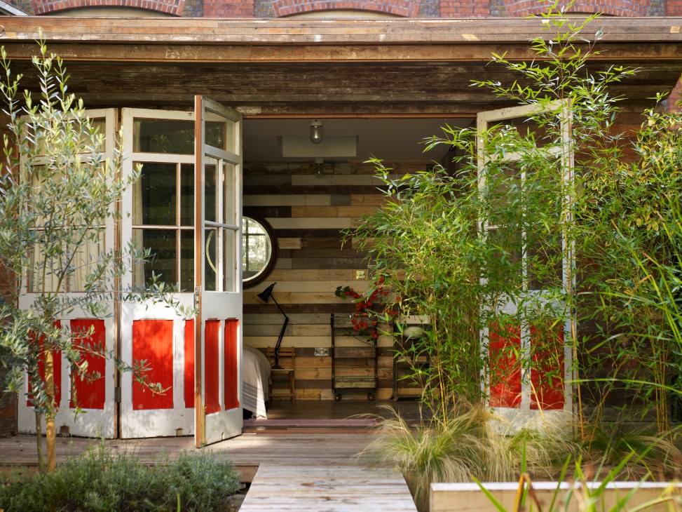 Garden cabin entrance with red and white doors, wooden beams, and bamboo plants framing the opening.