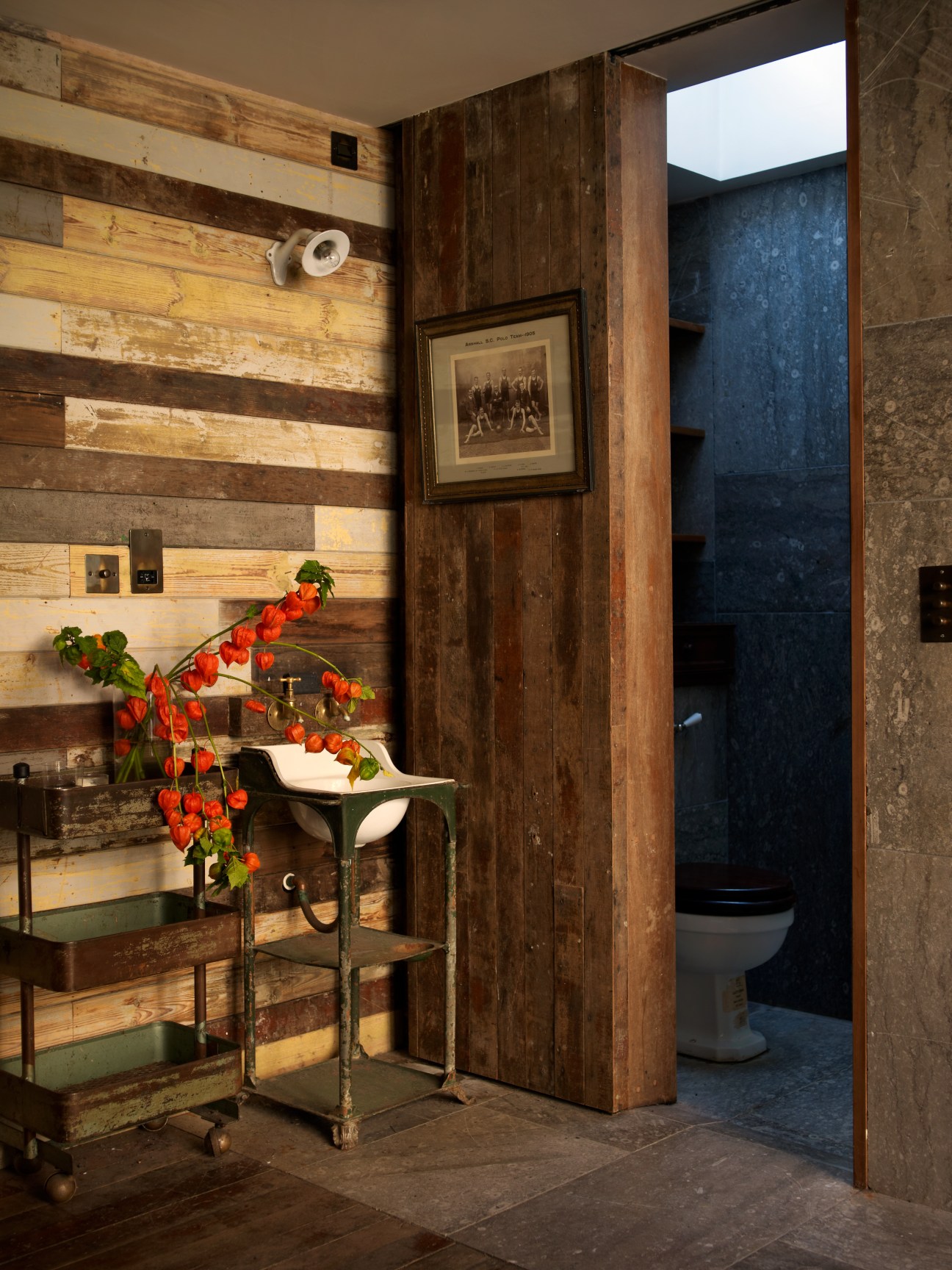 Bathroom interior with reclaimed wood wall paneling, vintage fixtures, and blue-grey concrete doorway.