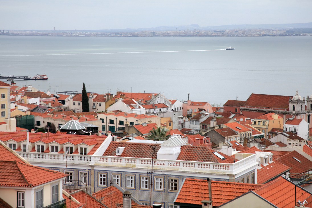 Aerial view of Lisbon's Lapa neighbourhood with terracotta roofs overlooking the Tejo river and opposite shoreline.